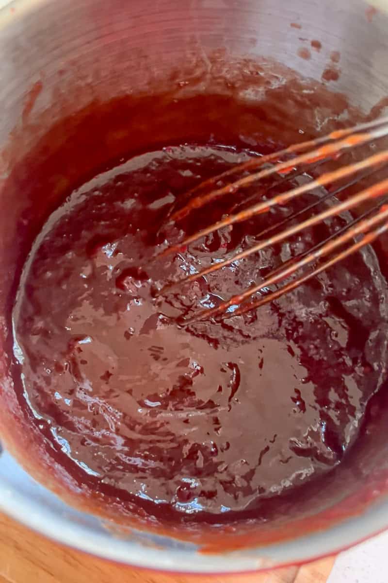 A saucepan of warm cranberry barbecue sauce being whisked until smooth.