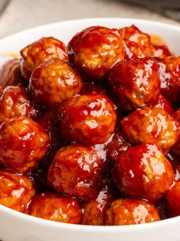 A close-up bowl full of glossy cranberry barbecue meatballs ready to serve.
