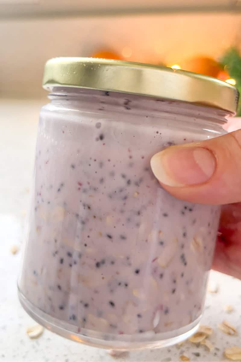 A hand holds a small glass jar filled with creamy cranberry overnight oats.