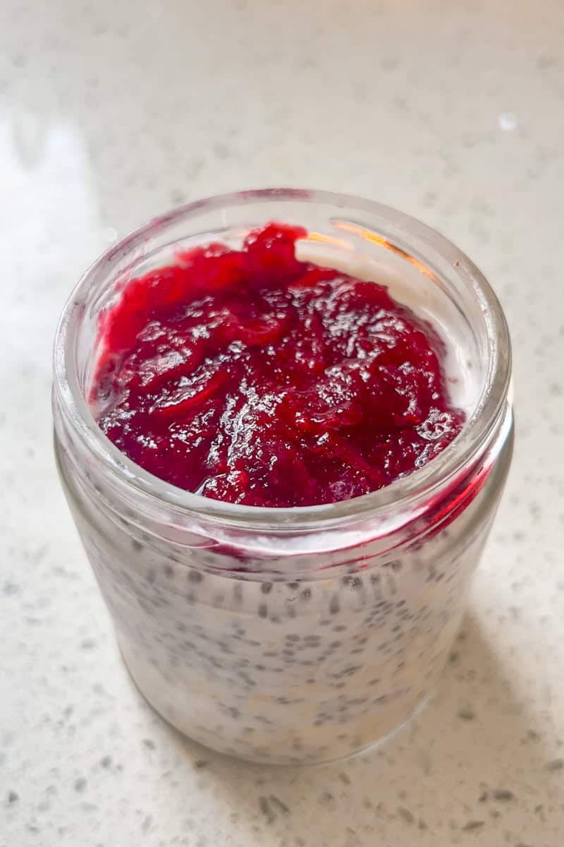 A glass jar of oats is topped with a layer of bright red cranberry sauce.