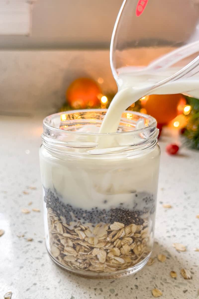 Milk is being poured into a jar layered with oats, chia seeds, and yogurt.
