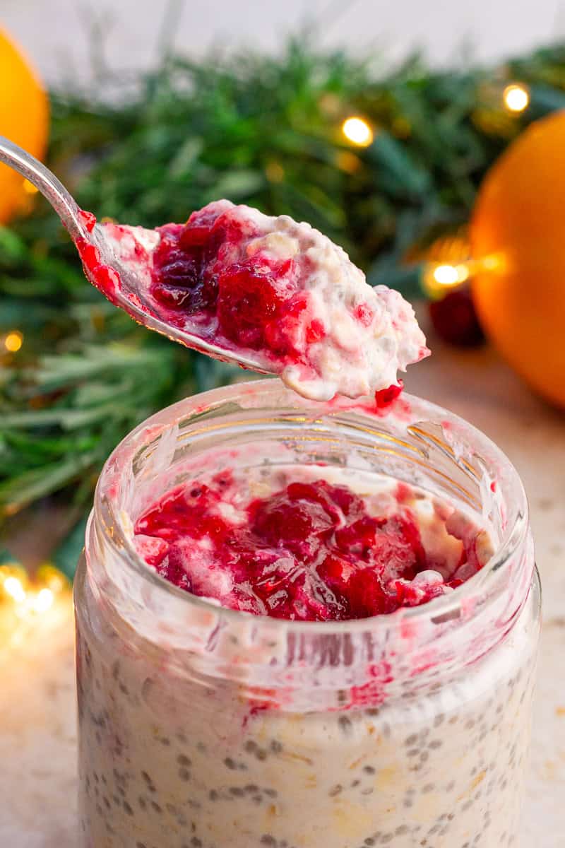 A spoon lifts a scoop of cranberry overnight oats topped with cranberry sauce from the jar.