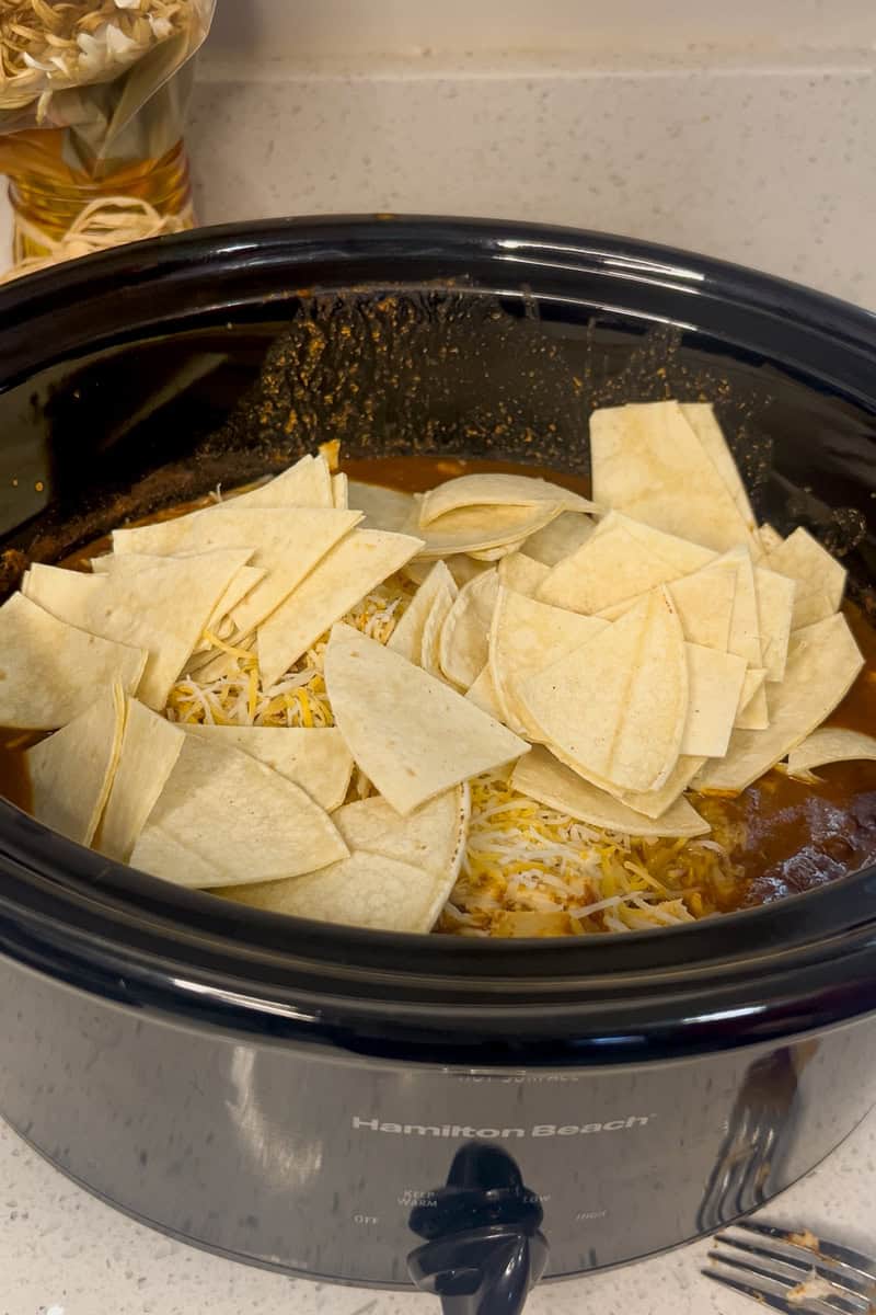 Corn tortilla pieces layered on top of chicken and cheese inside the slow cooker.