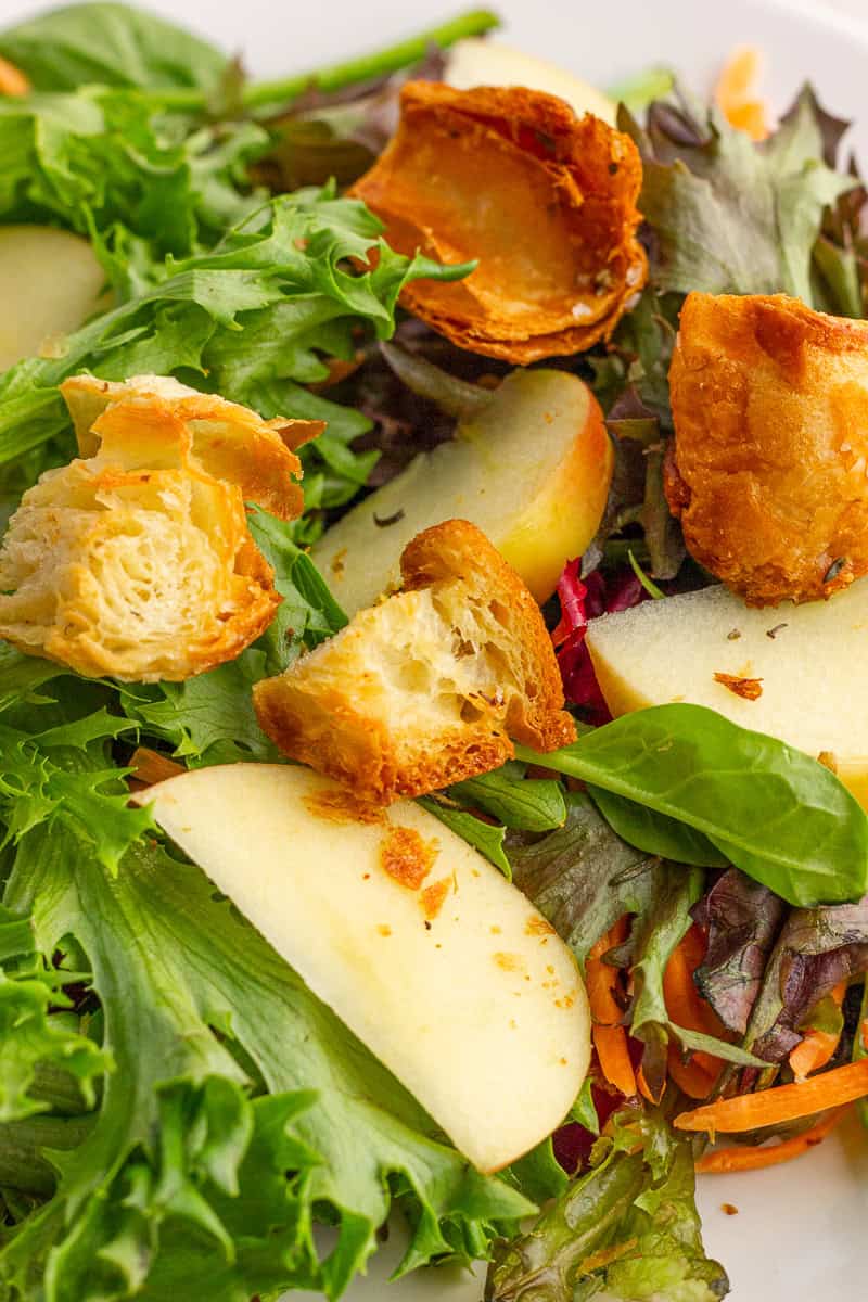 Crispy croissant croutons are sprinkled over a fresh salad with mixed greens and sliced apples.