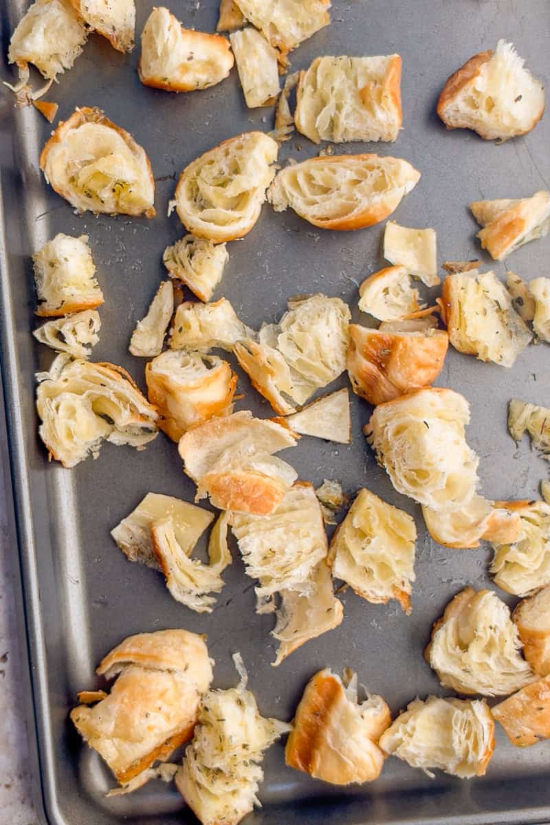 Unbaked croissant cubes are spread on a sheet pan before being toasted into croutons.