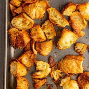 Crispy golden croissant croutons fill a sheet pan, showcasing their flaky and toasted texture.