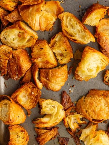 Crispy golden croissant croutons fill a sheet pan, showcasing their flaky and toasted texture.