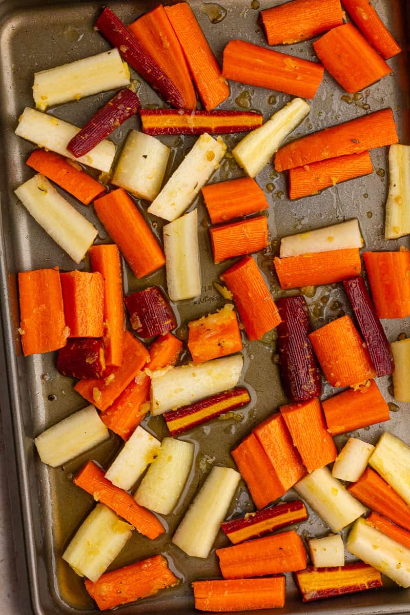 Chopped rainbow carrots are spread across a baking sheet and coated in glaze before roasting.