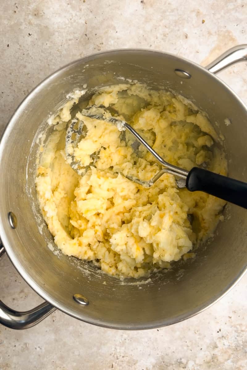 A pot of freshly mashed potatoes with a potato masher resting inside.