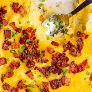 A top view of cheesy twice baked mashed potatoes topped with crispy bacon and chives.