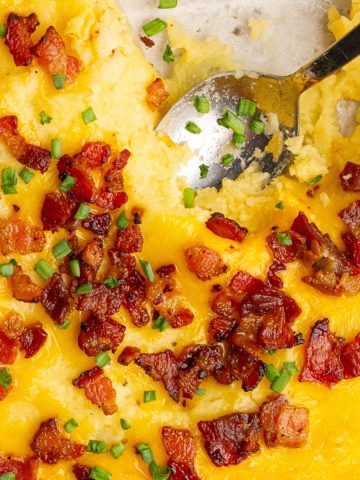 A top view of cheesy twice baked mashed potatoes topped with crispy bacon and chives.