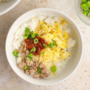 A breakfast rice bowl made with rice, scrambled eggs, turkey sausage, cheese, salsa, and green onions.