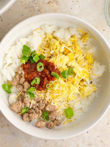A breakfast rice bowl made with rice, scrambled eggs, turkey sausage, cheese, salsa, and green onions.