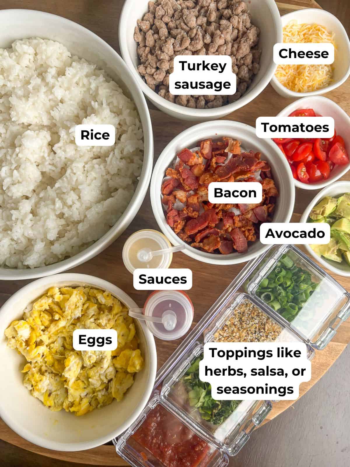 A breakfast rice bowl bar setup with bowls of Calrose rice, eggs, bacon, turkey sausage, tomatoes, cheese, sauces, and toppings.