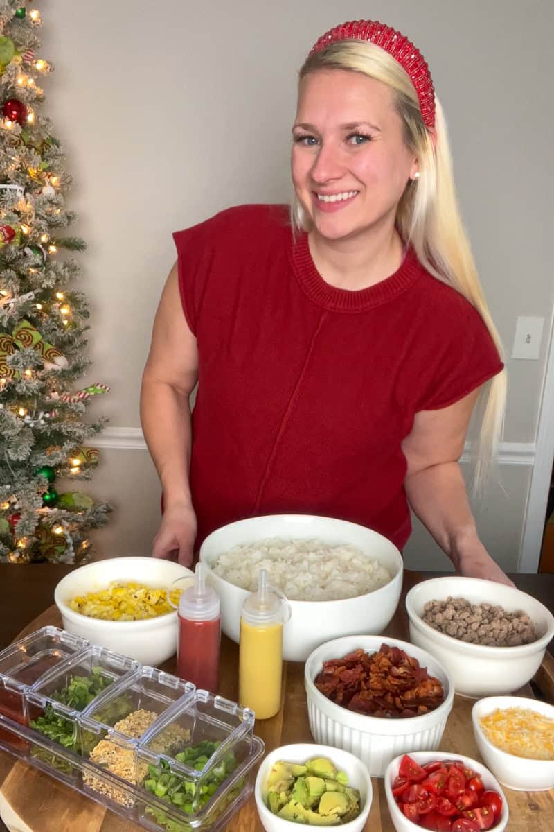 A blonde woman standing behind a breakfast rice bowl bar with various toppings ready to serve.