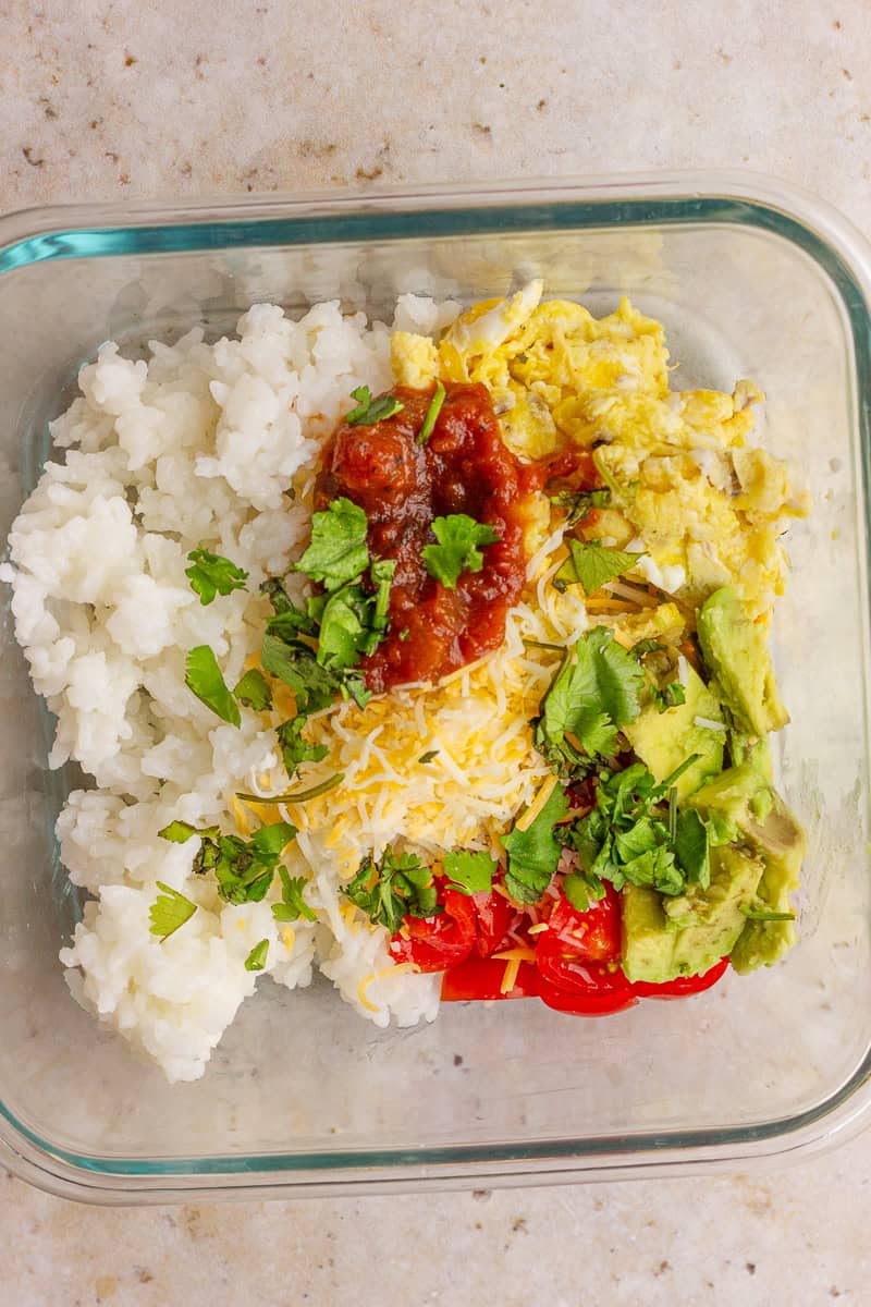 A fiesta-style breakfast rice bowl with eggs, cheese, salsa, avocado, and fresh cilantro.