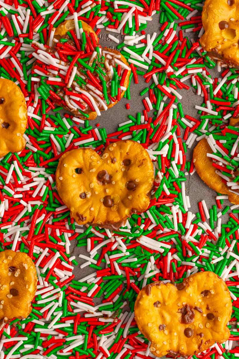 Several pretzel this rest on a baking sheet covered with festive Christmas sprinkles.