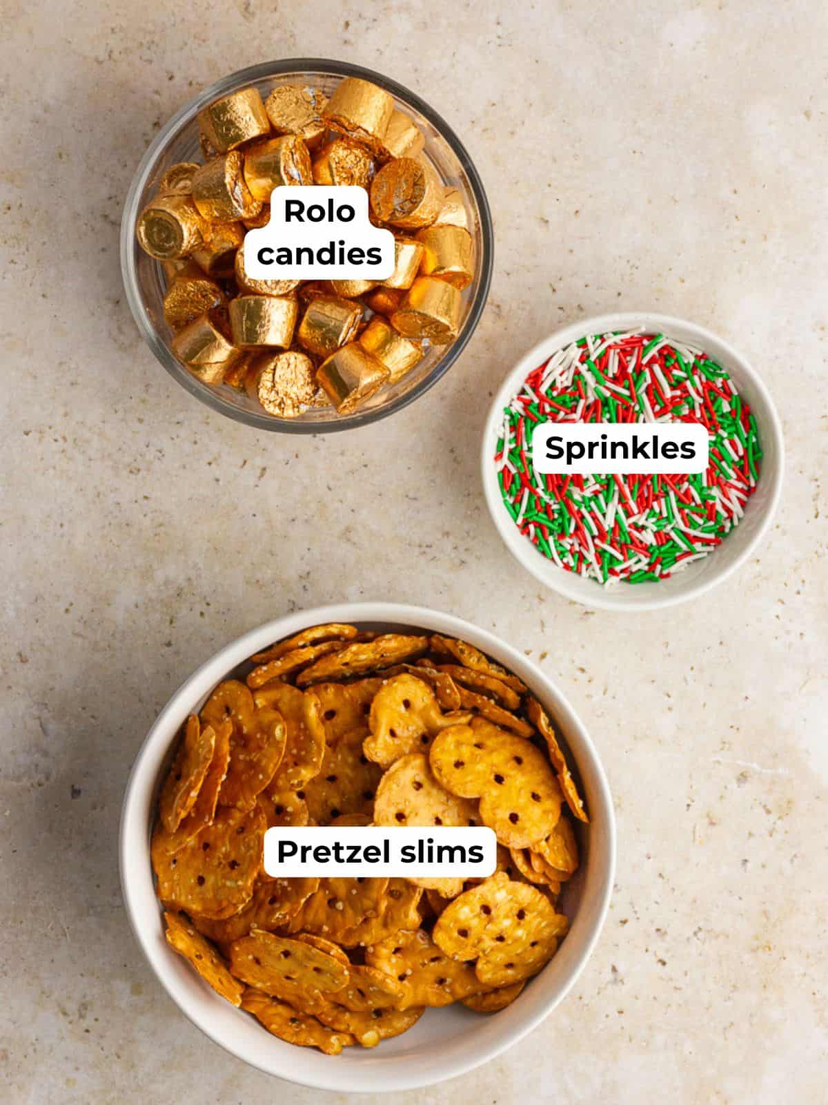 Bowls of pretzel slims, Rolo candies, and Christmas sprinkles are arranged neatly on a light surface.