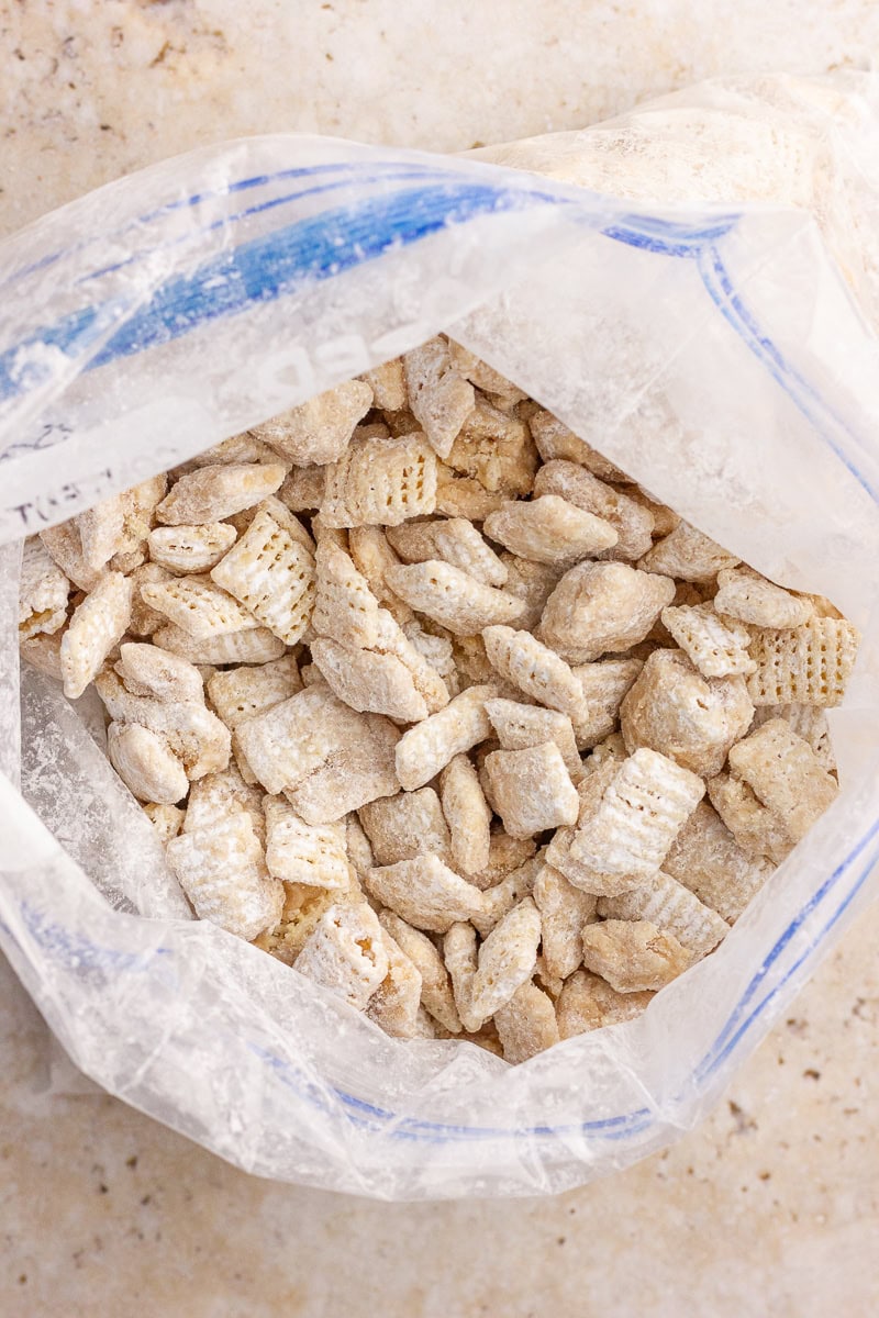 Cookie butter puppy chow coated in powdered sugar inside a zip-top bag on a light countertop.