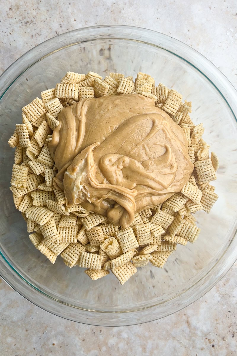 Melted cookie butter mixture poured over Rice Chex cereal in a glass mixing bowl.