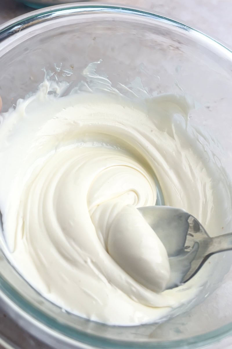 Smooth melted white chocolate in a glass bowl with a spoon.