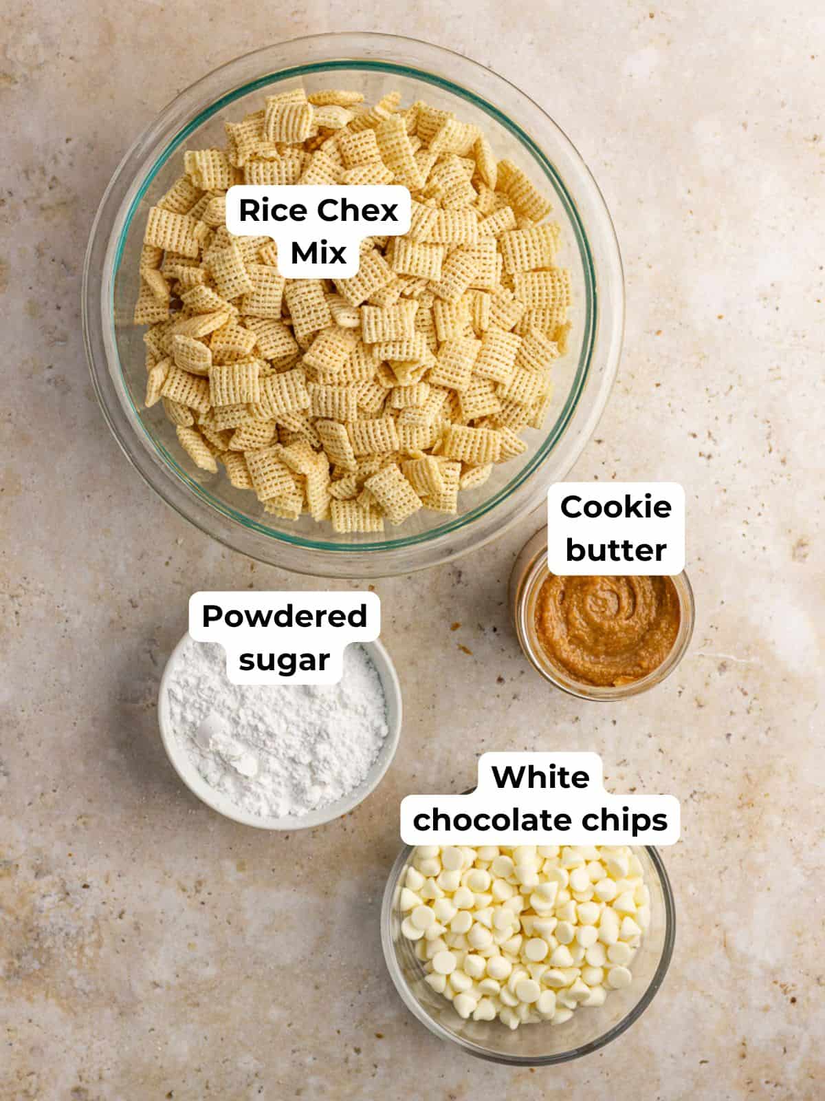 Cookie butter puppy chow ingredients arranged on a countertop, including cereal, cookie butter, white chocolate chips, and powdered sugar.