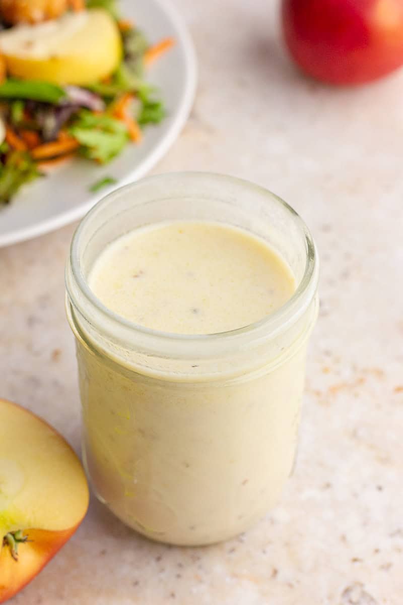 A top view of a mason jar filled with creamy apple cider vinaigrette with a salad blurred in the background.