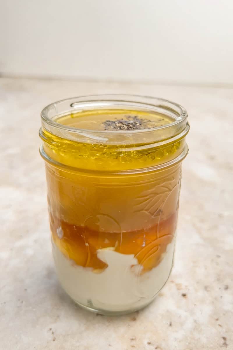 Ingredients for the vinaigrette are layered in a mason jar before shaking, showing yogurt, honey, vinegar, and oil.