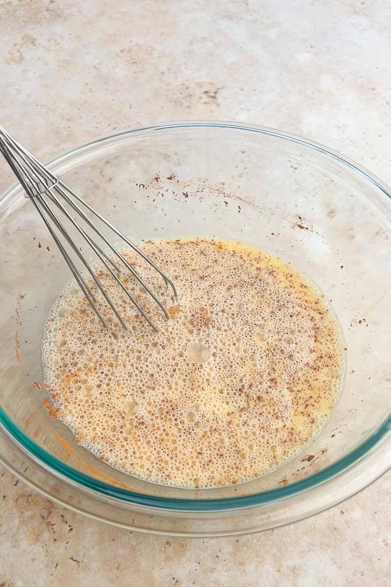 A bowl of eggs, egg whites, milk, and cinnamon being whisked together until smooth.
