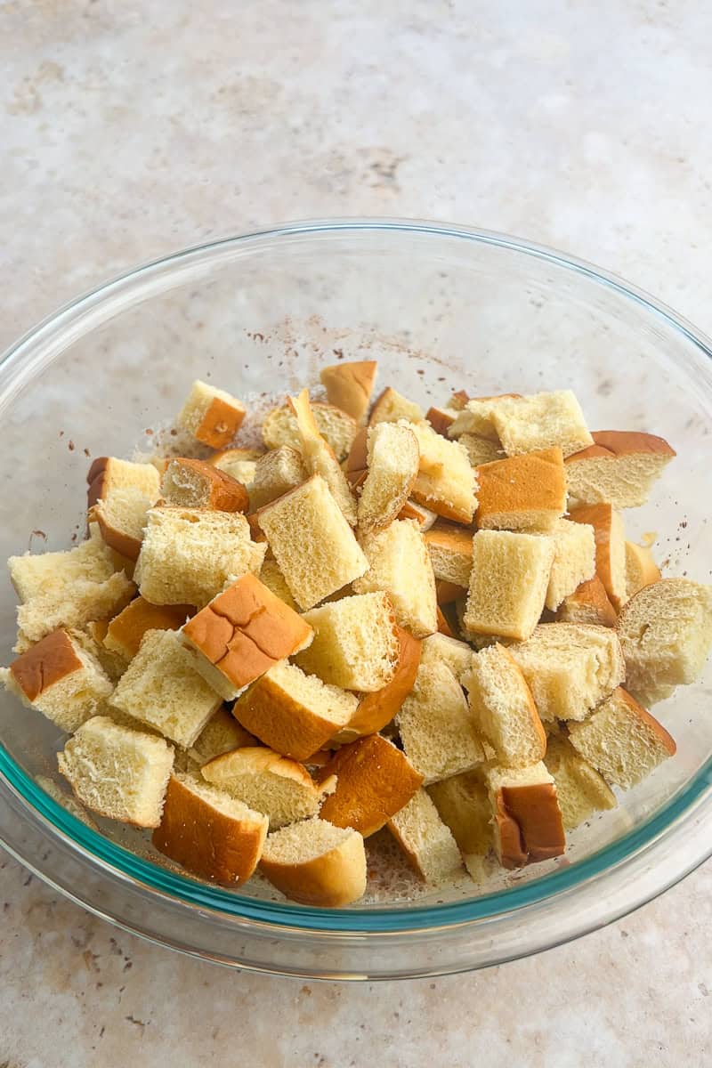 Chunks of bread sitting in the bowl of custard as they are gently stirred to coat.
