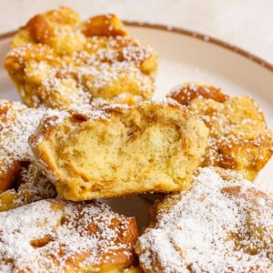 A close up of several powdered sugar coated french toast cups arranged on a plate, with one cut open to show the texture.