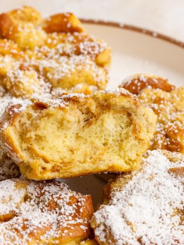 A close up of several powdered sugar coated french toast cups arranged on a plate, with one cut open to show the texture.