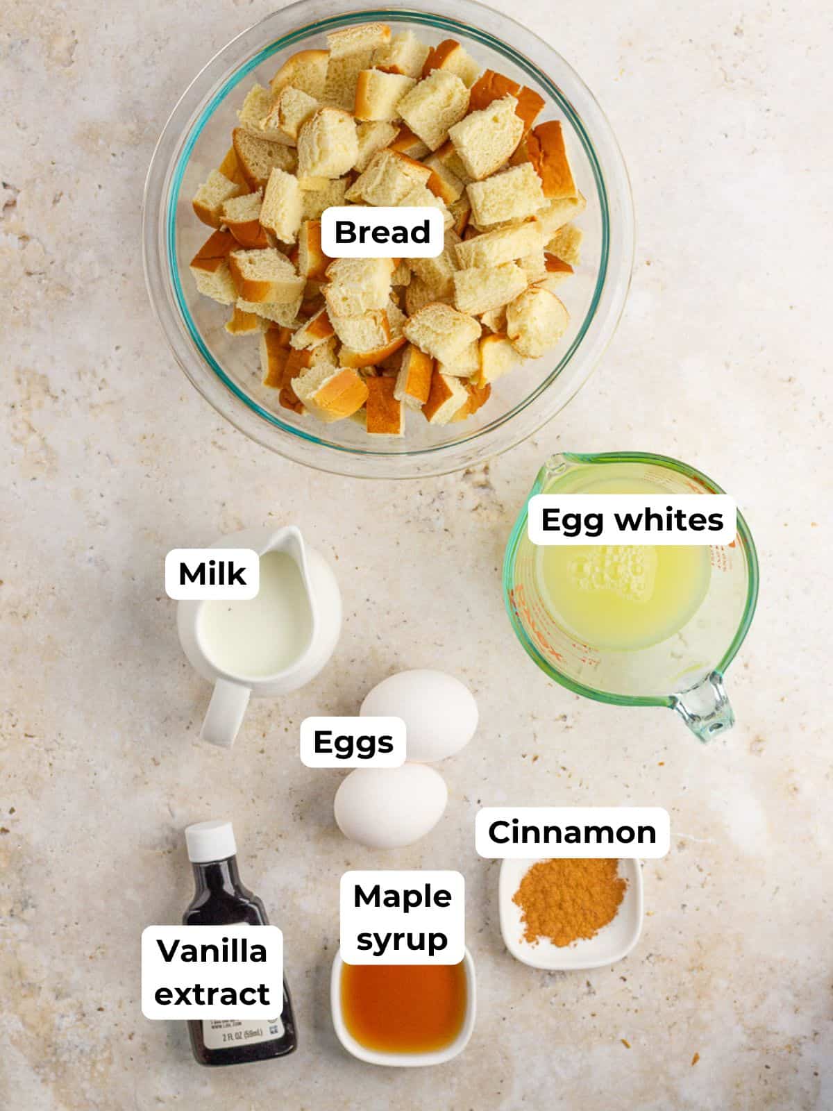 A top down view of the bread, eggs, milk, maple syrup, cinnamon, and vanilla arranged on a countertop.