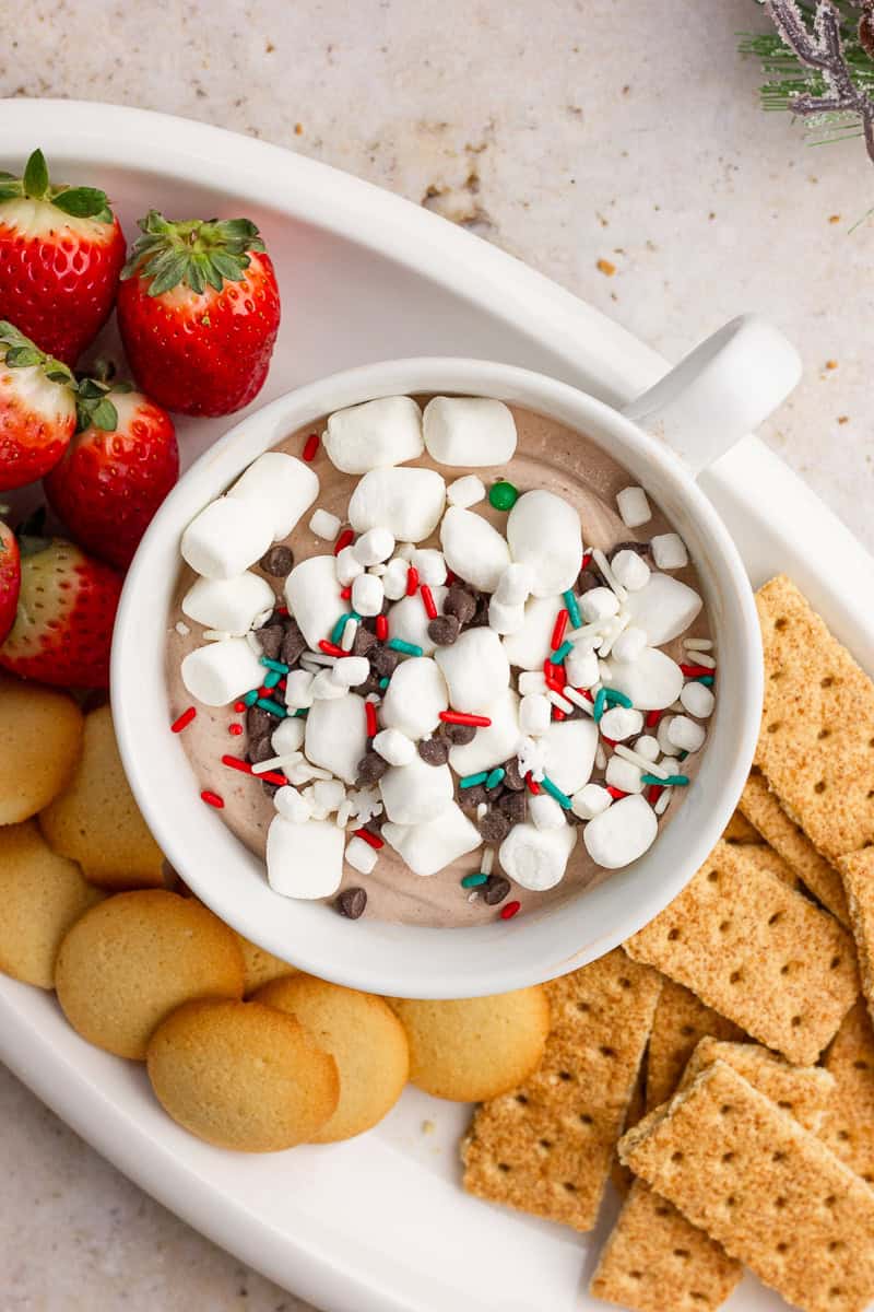 Overhead view of hot cocoa dip garnished with marshmallows and sprinkles on a dessert platter with strawberries and cookies.