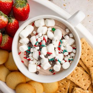 Overhead view of hot cocoa dip topped with marshmallows and chocolate chips surrounded by cookies and graham crackers.