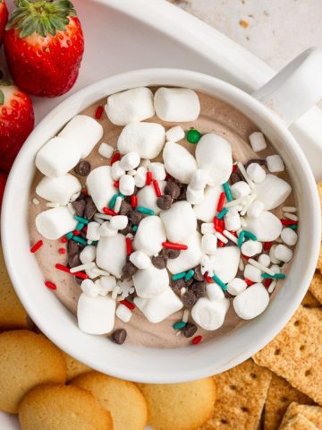 Overhead view of hot cocoa dip topped with marshmallows and chocolate chips surrounded by cookies and graham crackers.