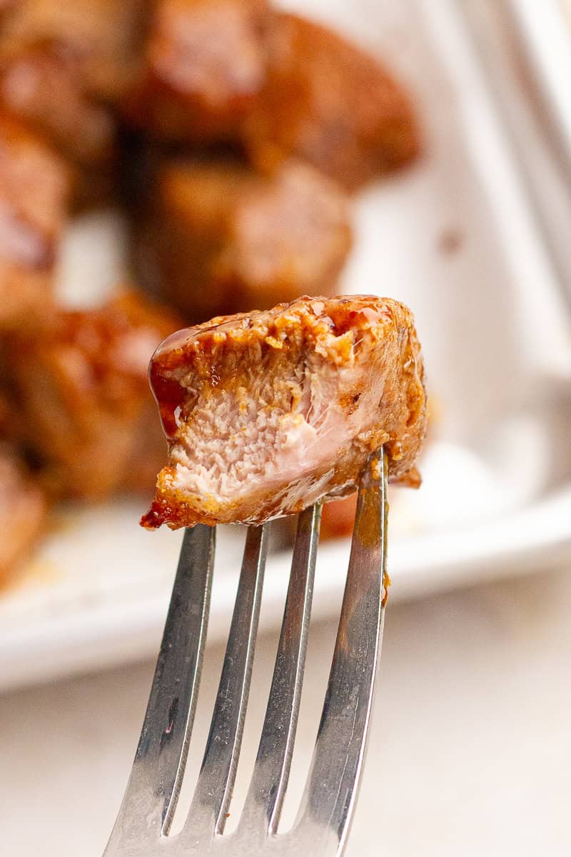 A fork holds a juicy pork tenderloin bite to show its tender, perfectly cooked center.