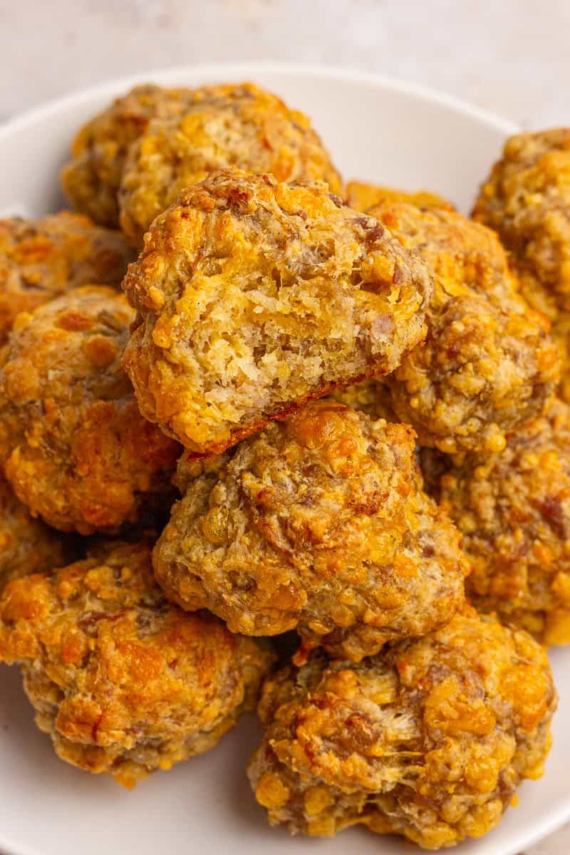 A sausage ball with a bite taken out sits on top of a plate of baked sausage balls.