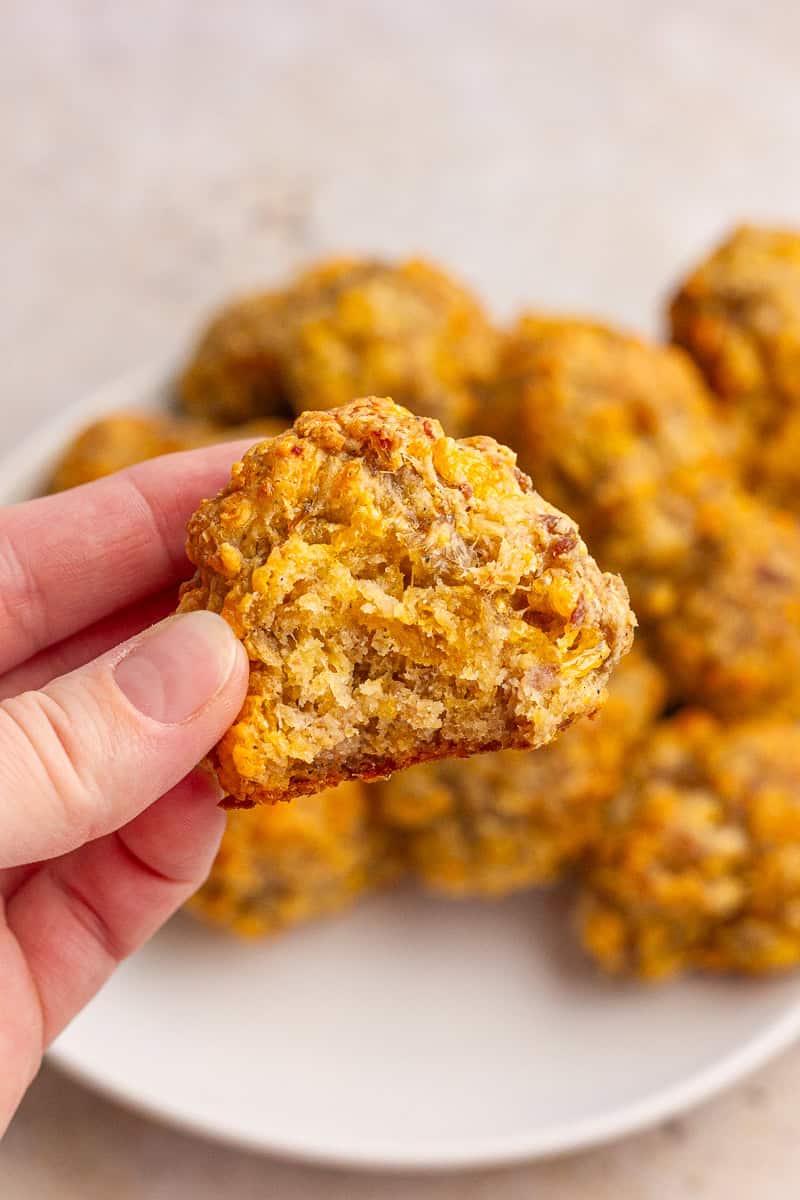 A hand holds a sausage ball with a bite taken out to show the soft, cheesy interior.
