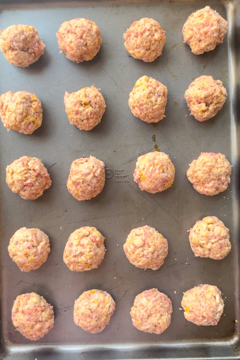 Unbaked sausage balls are evenly spaced on a baking sheet before going into the oven.