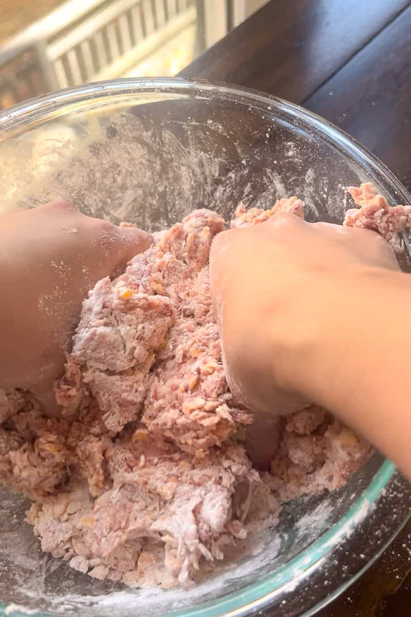 Hands mix the sausage ball dough in a large glass bowl.