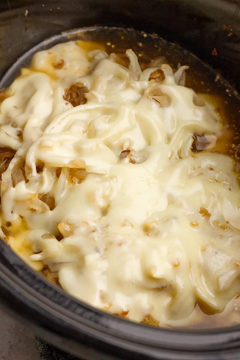 Melted Swiss cheese covers tender chicken and onions inside a slow cooker.