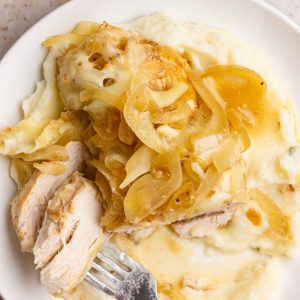 French onion chicken with onions and melted cheese is served over mashed potatoes.