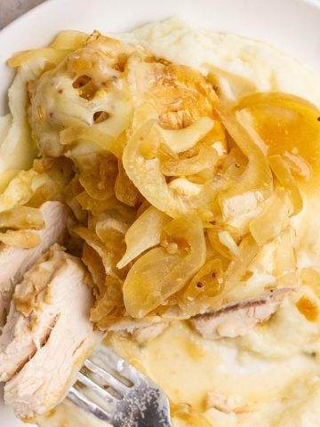 French onion chicken with onions and melted cheese is served over mashed potatoes.