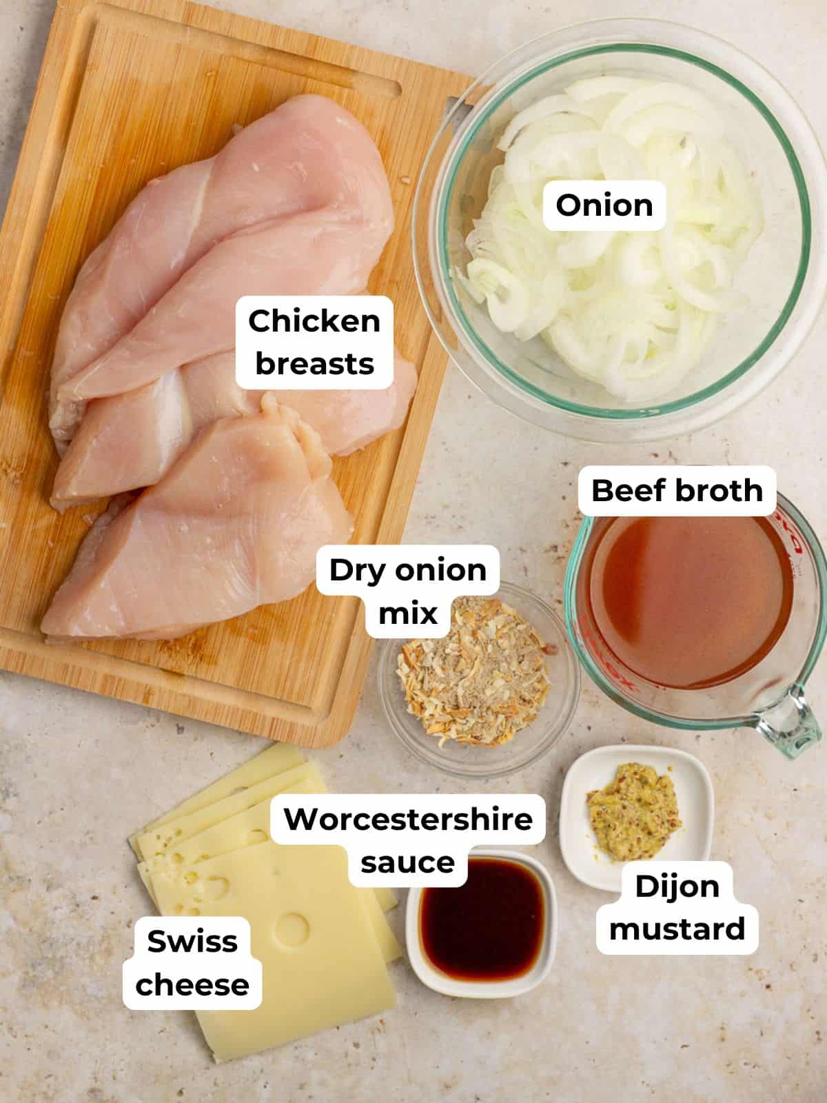 All recipe ingredients including chicken, onions, broth, soup mix, mustard, Worcestershire, and cheese are arranged on a countertop.
