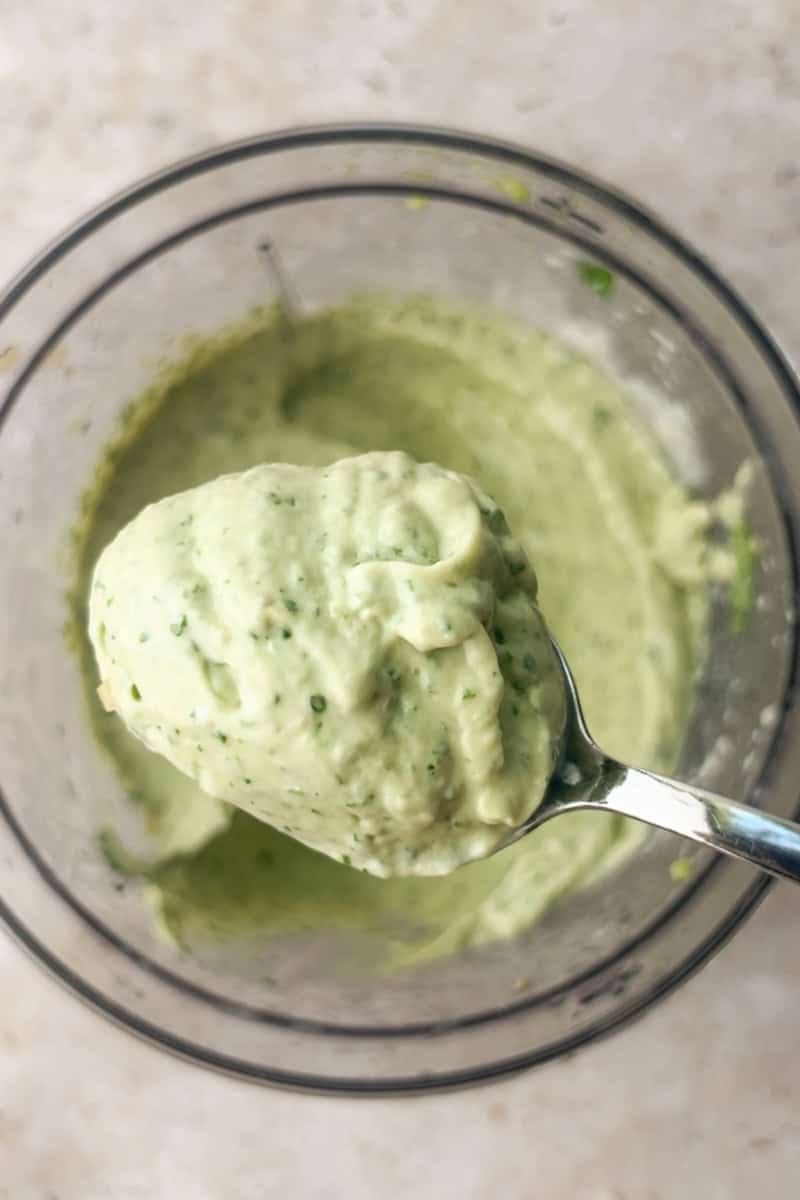 A spoonful of thick and creamy avocado lime crema lifted from a food processor bowl.