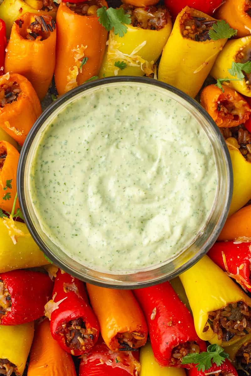 Avocado lime crema served in a bowl surrounded by colorful stuffed mini peppers on a platter.