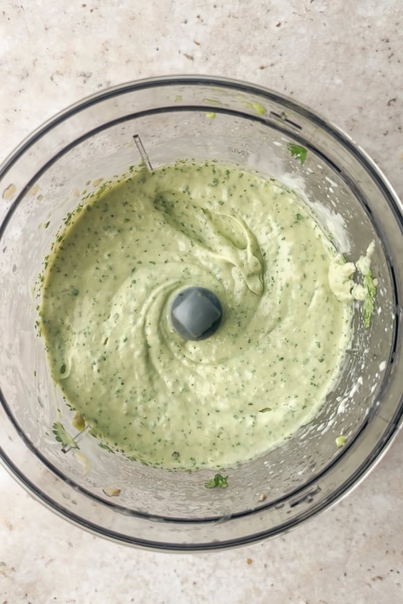 Avocado lime crema blended smooth inside a food processor bowl.