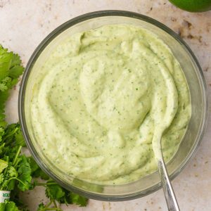 A close-up of smooth and creamy avocado lime crema in a glass bowl with a spoon.