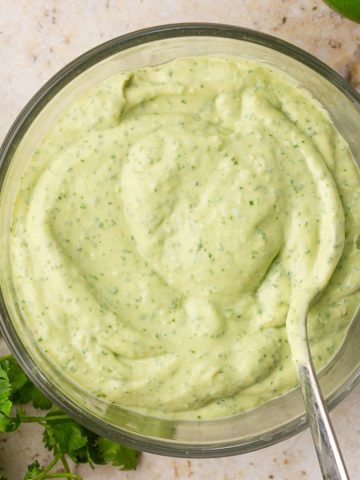 A close-up of smooth and creamy avocado lime crema in a glass bowl with a spoon.